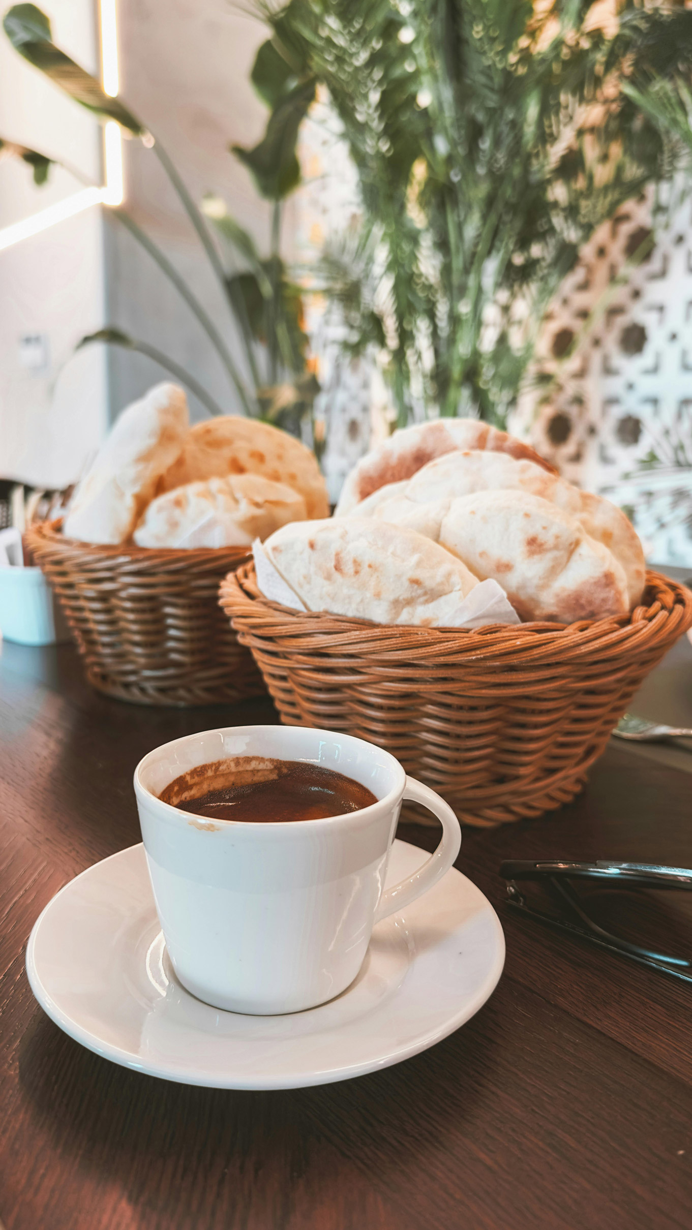 Small cup of coffee next to baskets of bread